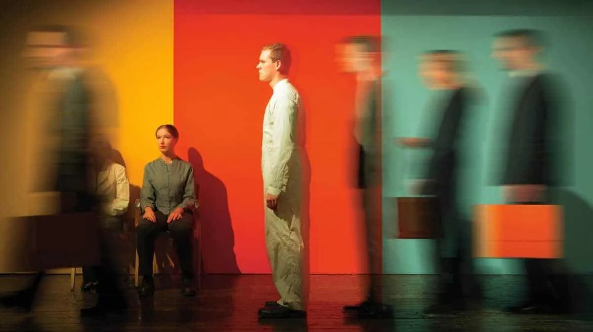 People waiting in a colourful room, some blurred, one person sitting, one standing.