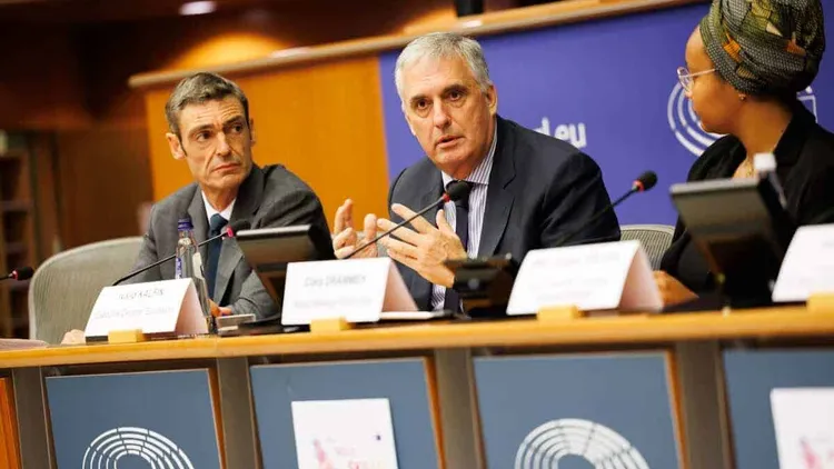 Three individuals at a panel discussion, European Parliament setting.
